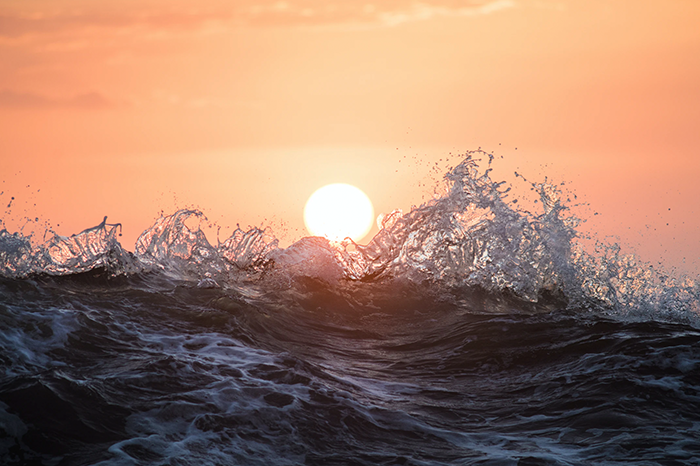 sun setting into an ocean wave