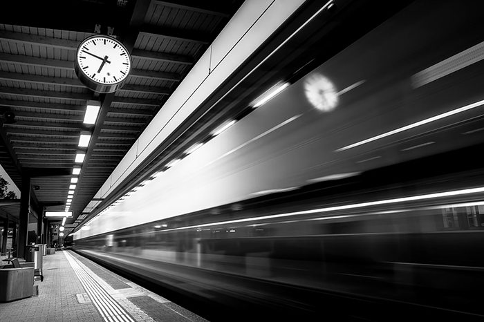 Train speeding by a station with a clock in focus